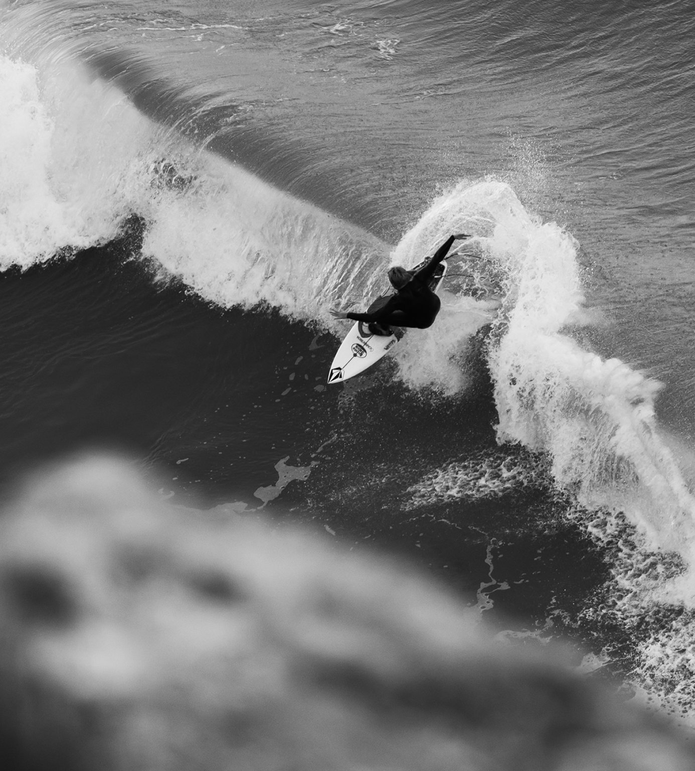 A black and white photo of a surfer riding a wave, with dynamic motion captured as the surfer carves and spray flies off the board