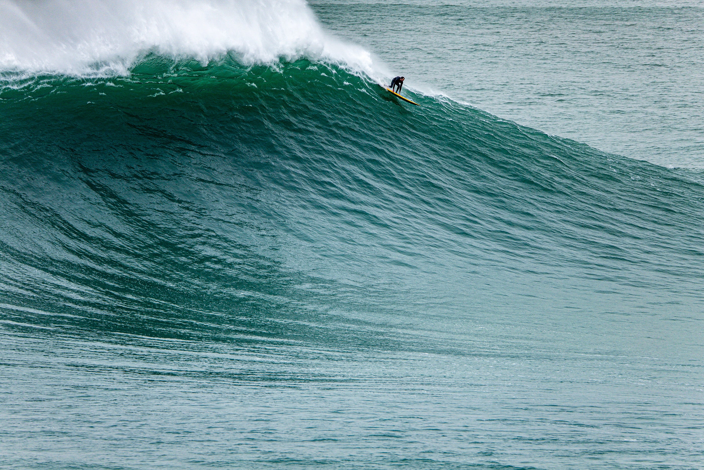 A surfer taking off on a massive wave, just as it begins to break