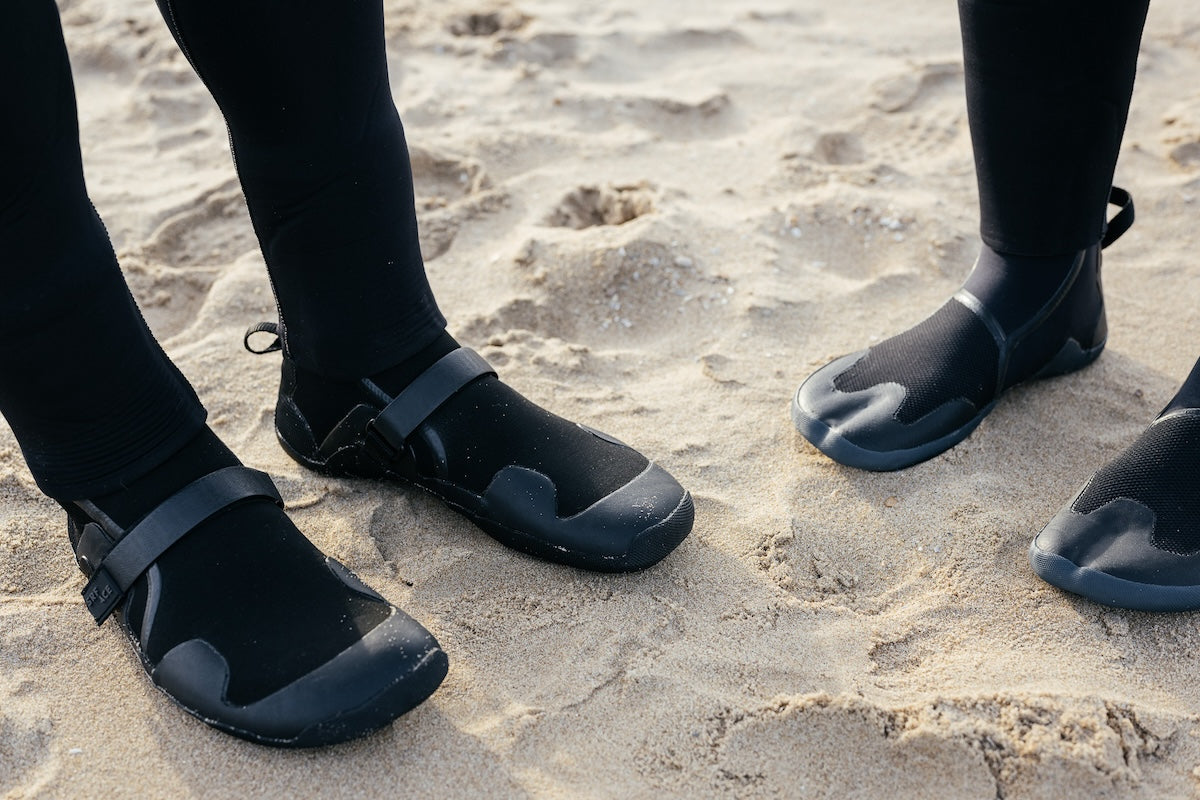 Two surfers wearing different types of SRFACE boots on the beach
