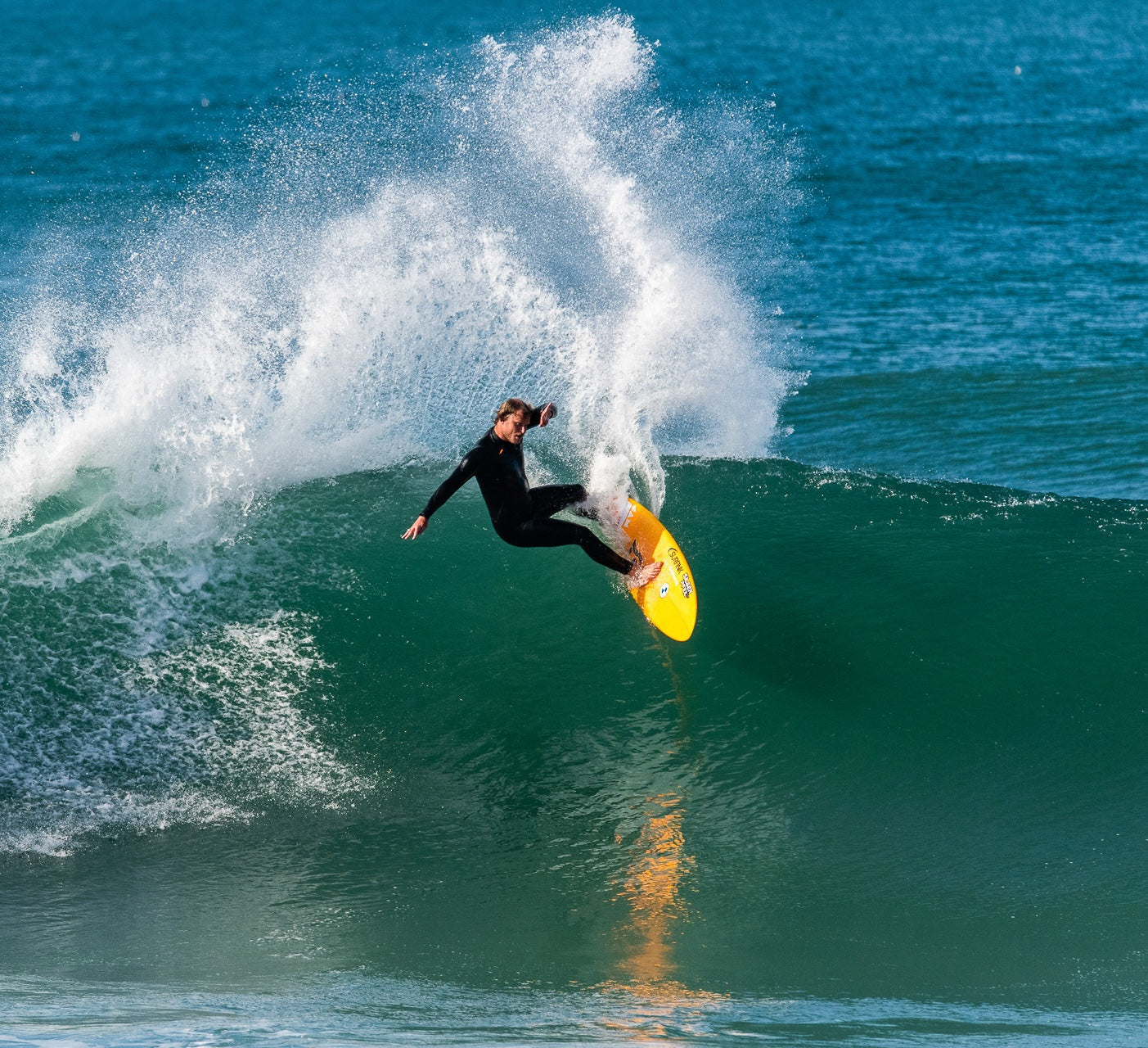 A surfer performing a top turn on a clear wave, carving sharply along the wave's face under the bright sunlight