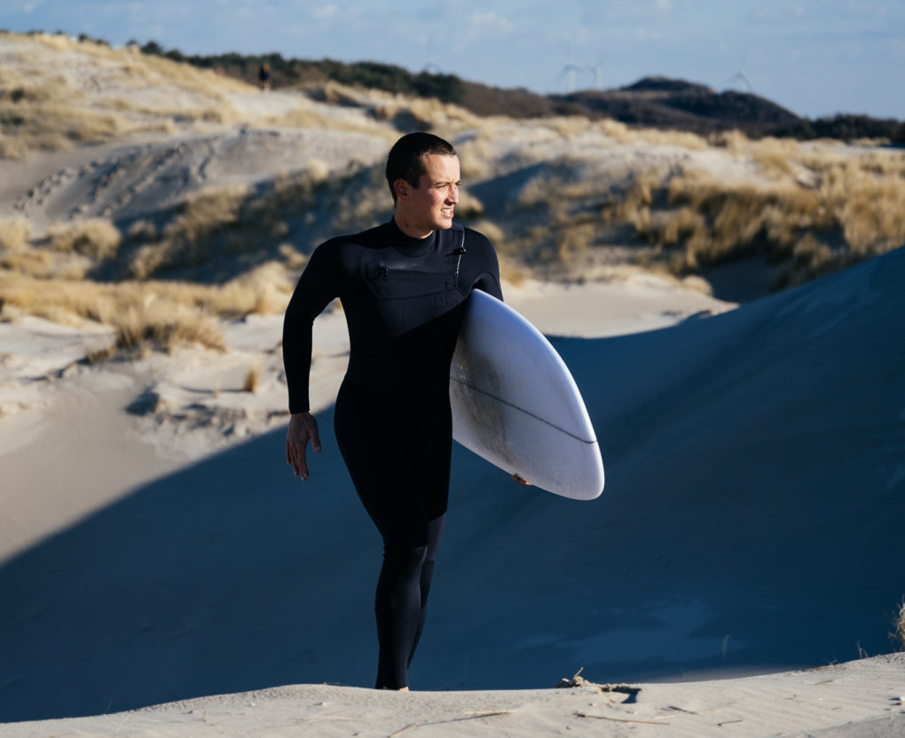 A man walking along the beach, carrying a surfboard, ready to go surfing
