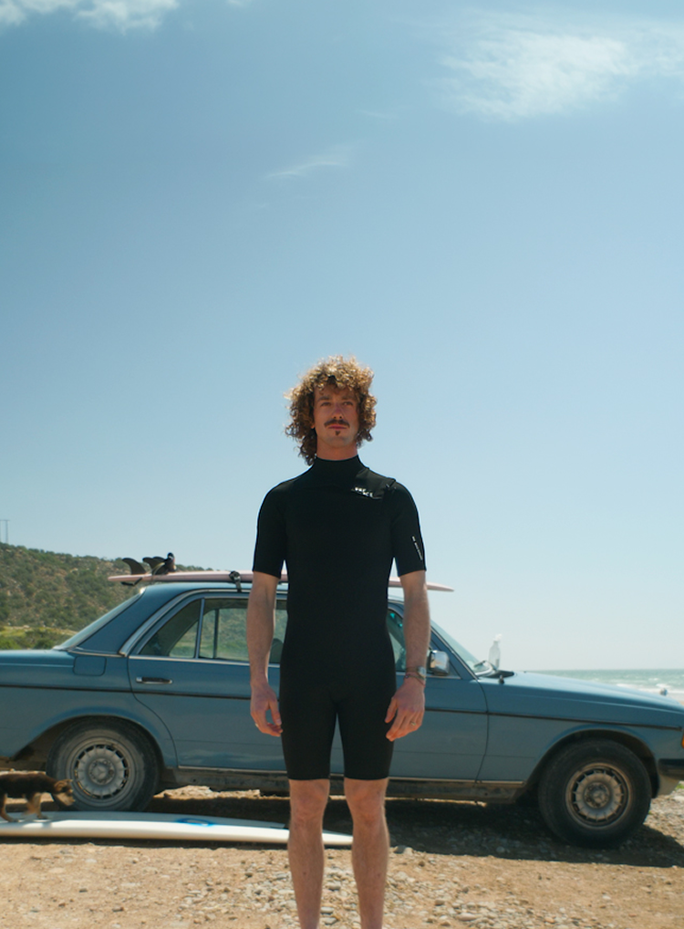 Surfer standing in front of a car on the beach