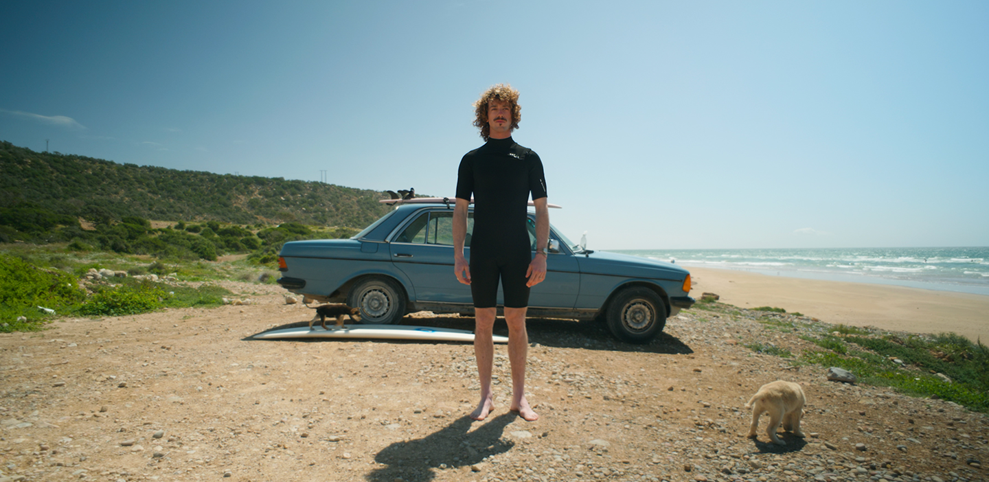 Surfer standing in front of a car on the beach